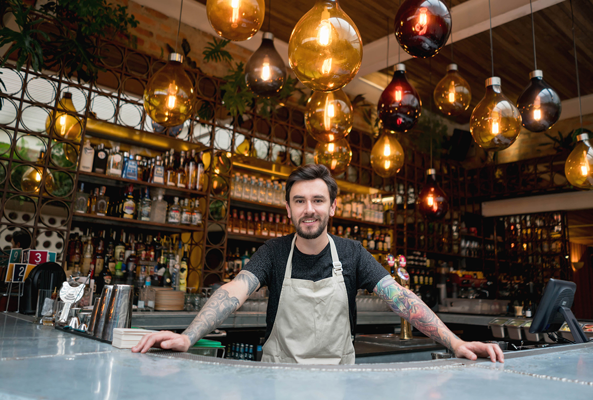 bar owner posing in front of bar with arms spread