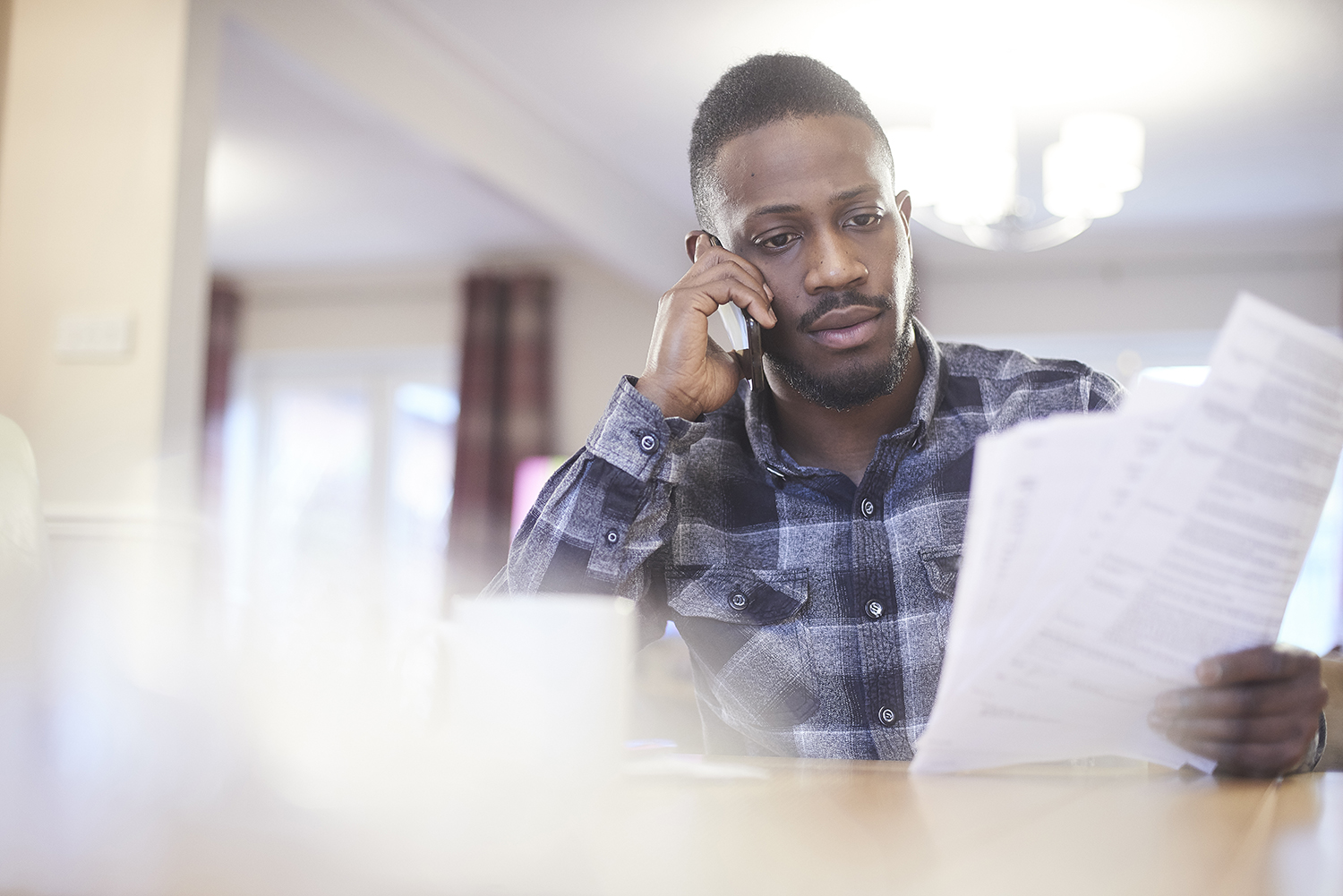 Young black male on the phone in a home environment holding paperwork