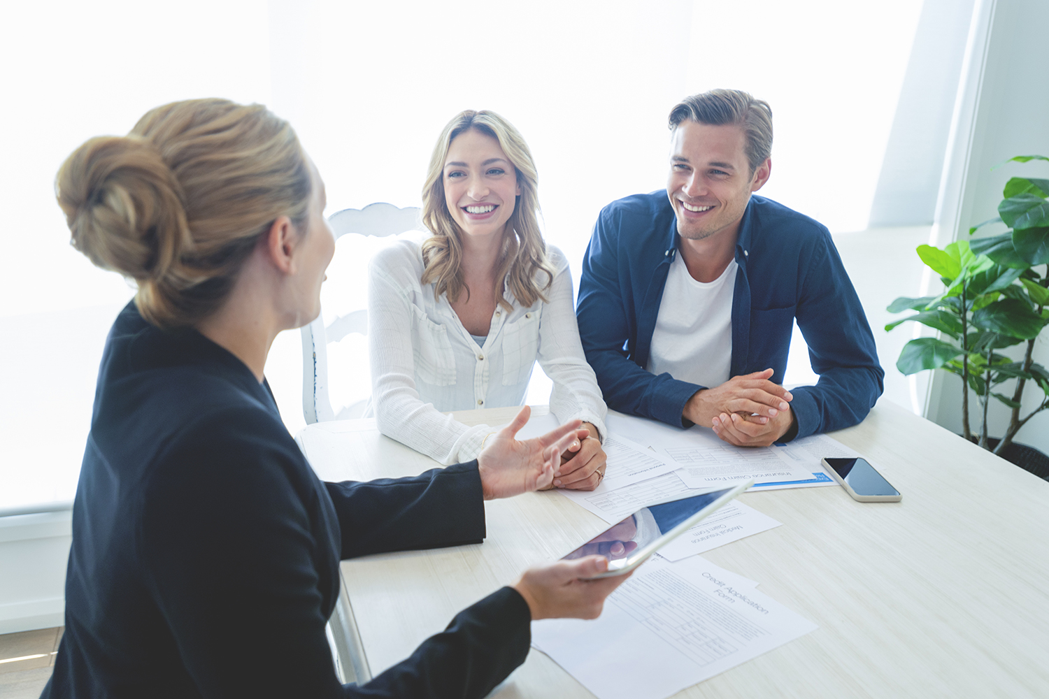 Insurance agent with couple looking through documents. The agent is holding a digital tablet. Couple are casually dressed. They sitting at a table at home and are looking a little happy and smiling.